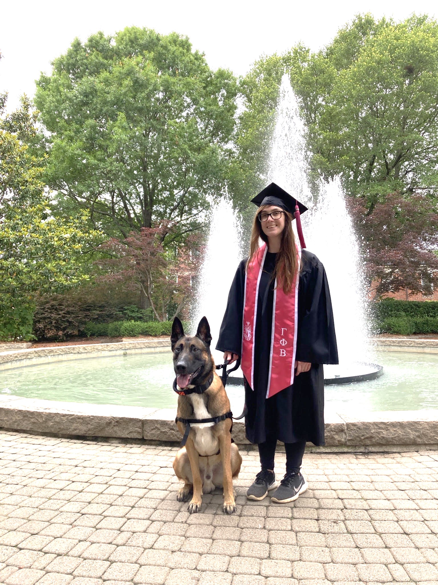 Bailey in UGA cap and gown with dog in front of fountain 